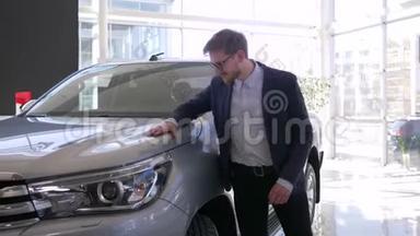 购买汽车，年轻的买家戴着<strong>眼镜</strong>的男人欣然地抚摸着新车，并给予积极的姿态